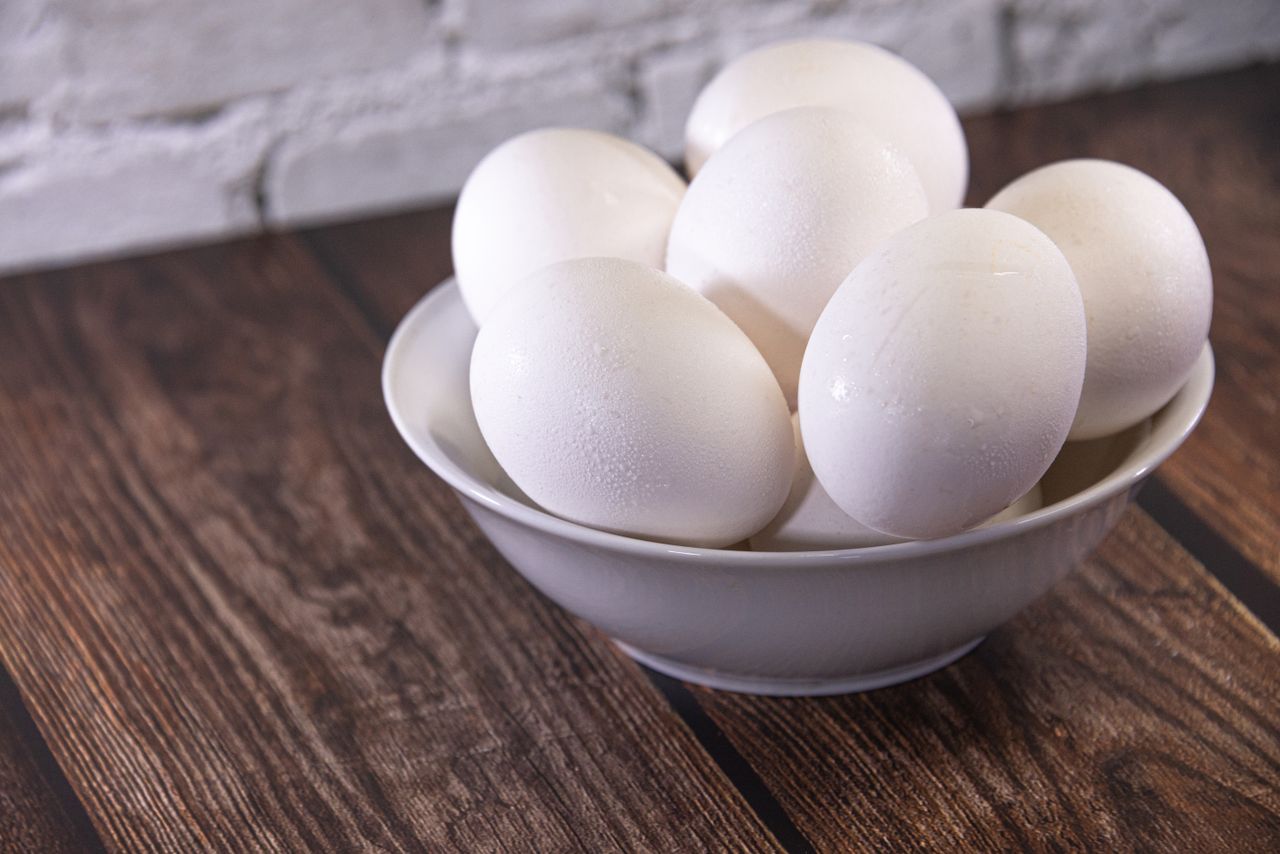 A close-up of fresh white eggs in a ceramic bowl on a rustic wooden table.