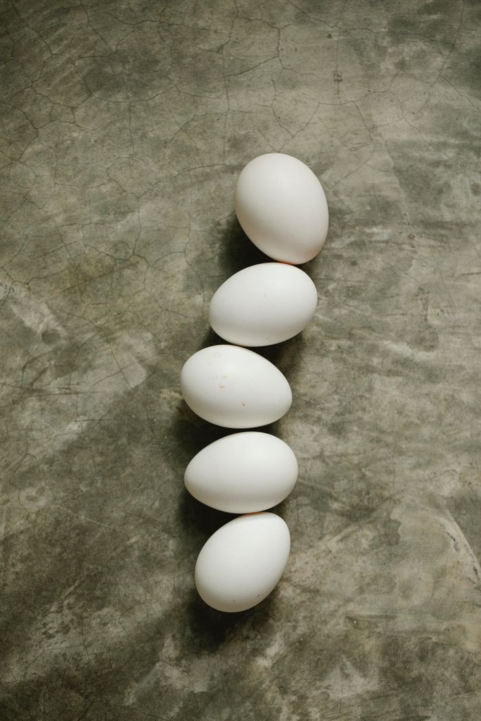 From above of whole raw white chicken eggs placed in row on gray tabletop in kitchen