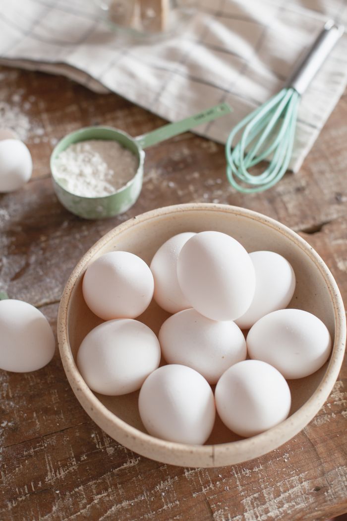 A bowl of white eggs on a wooden table with baking tools creates a cozy kitchen scene.